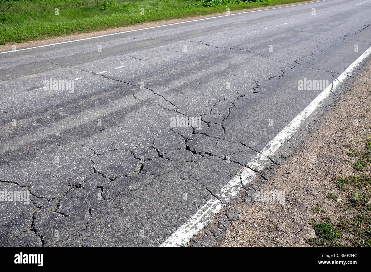 Suburban road in bad condition needs repairs. Rural car road with broken asphalt in sunny summer day diagonal view Stock Photo