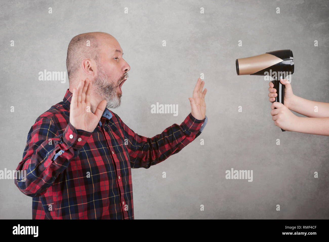 Surprised adult bald man next to a hair dryer against gray background Stock Photo