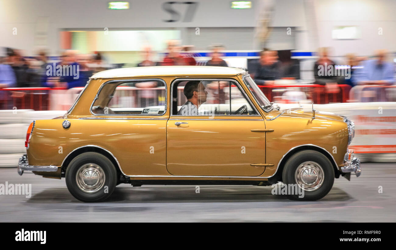ExCel, London, UK, 14th Feb 2019. A vintage gold Mini Cooper races down the Grand Avenue track ,The London Classic Car Show 2019 opens at ExCel Exhibition Centre in London Docklands. The show  brings together classic car owners, collectors, experts and enthusiast with dealers, manufacturers and car clubs in a celebration of motoring and classic cars. Credit: Imageplotter News and Sports/Alamy Live News Stock Photo