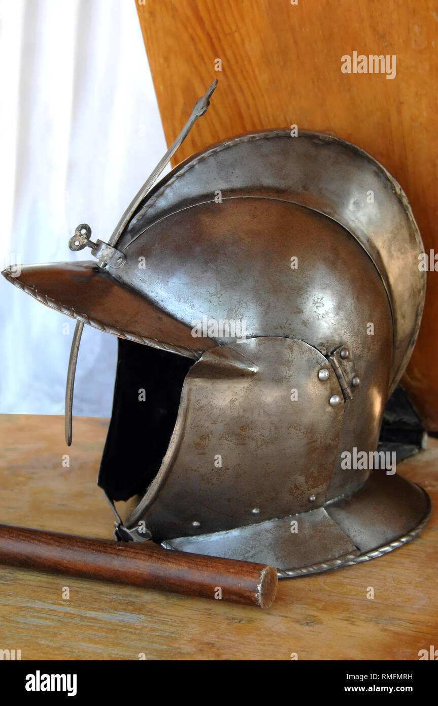 Helmet, like one worn by Spanish conquistadors, sits on a table.  Meltal is dented and weathered. Stock Photo