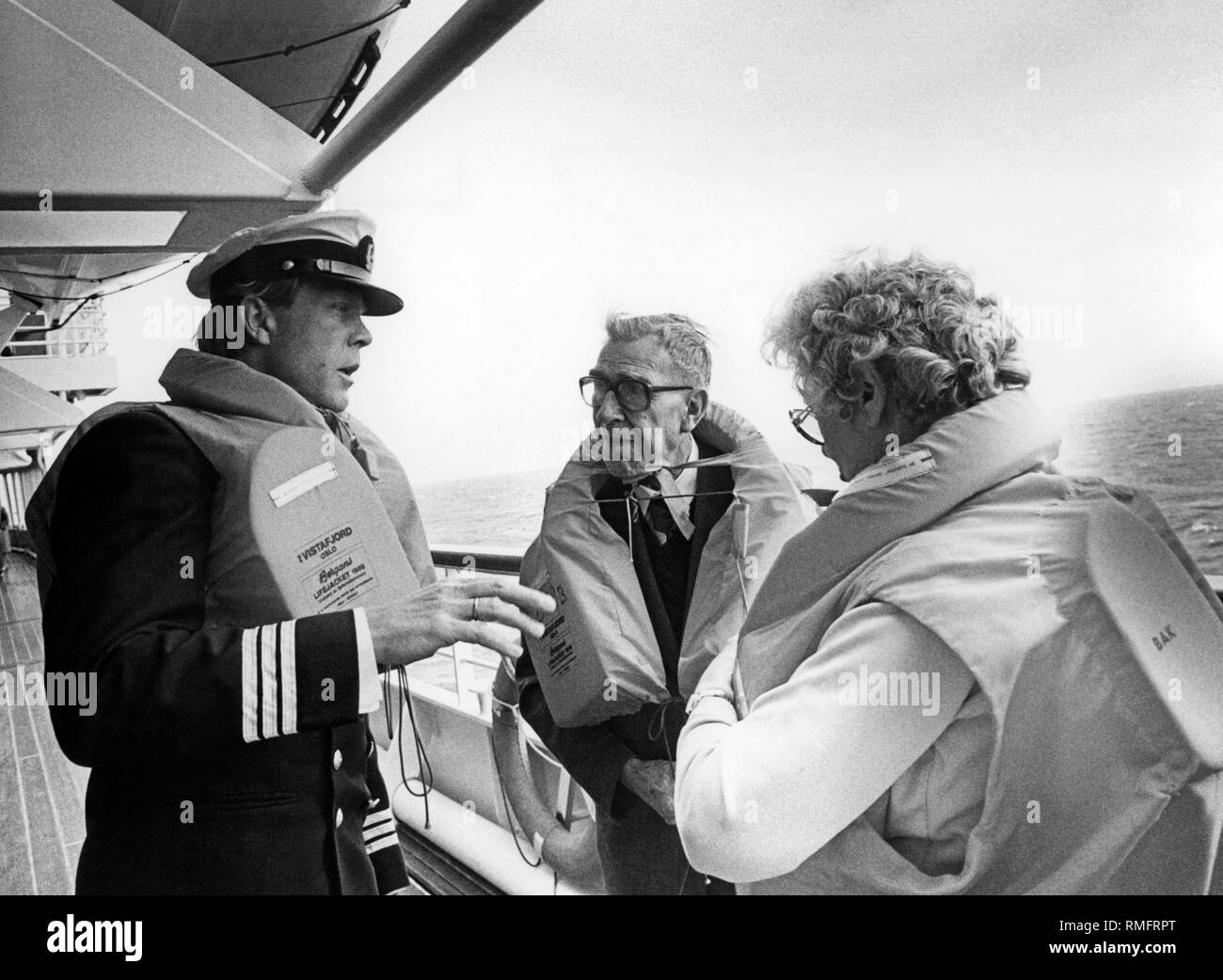 A crew member explains the functioning of the lifejackets to two passengers. Stock Photo