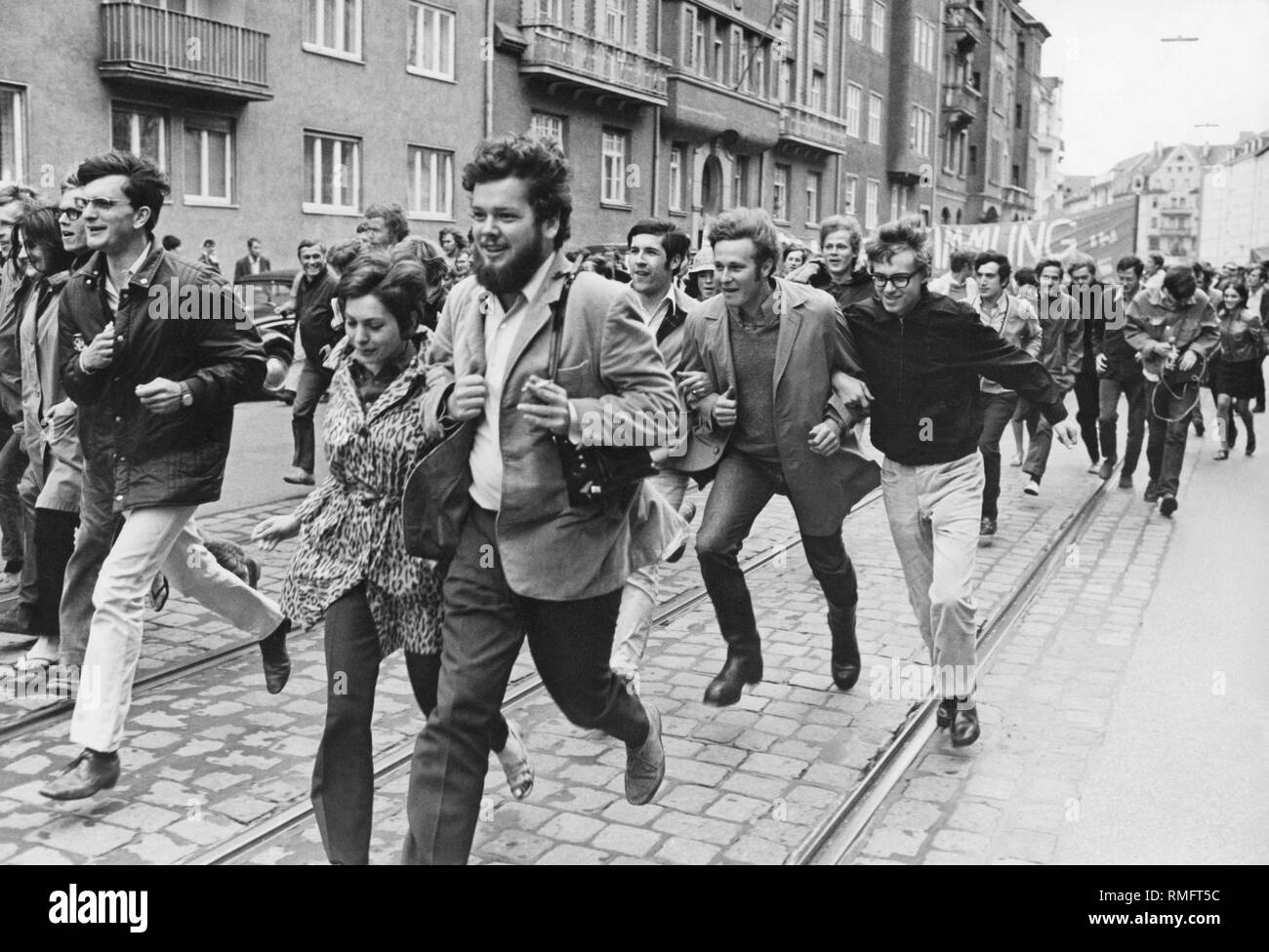 A group of demonstrating students are running down a Munich street. Stock Photo
