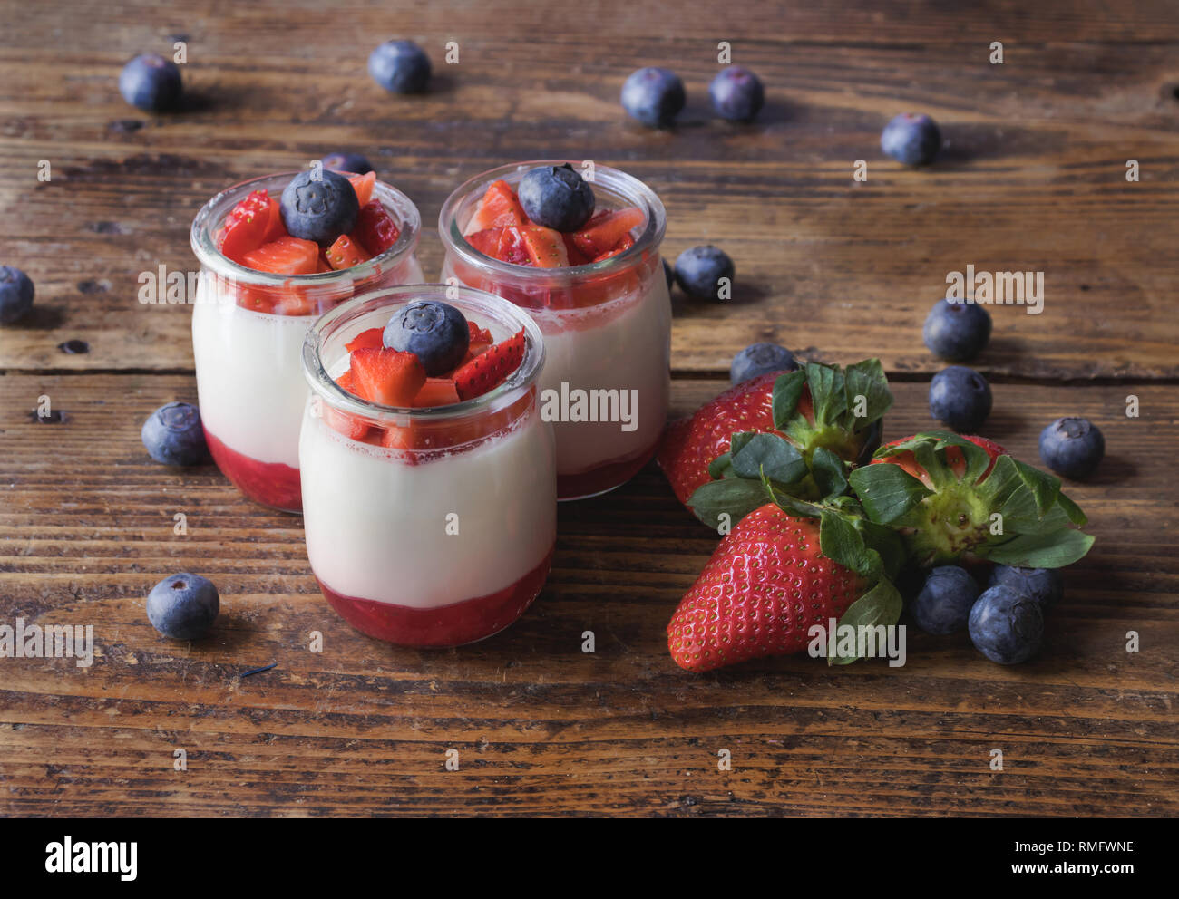 Delicious homemade yogurt with strawberry jam and sliced strawberries and blueberries, on a wooden board Stock Photo
