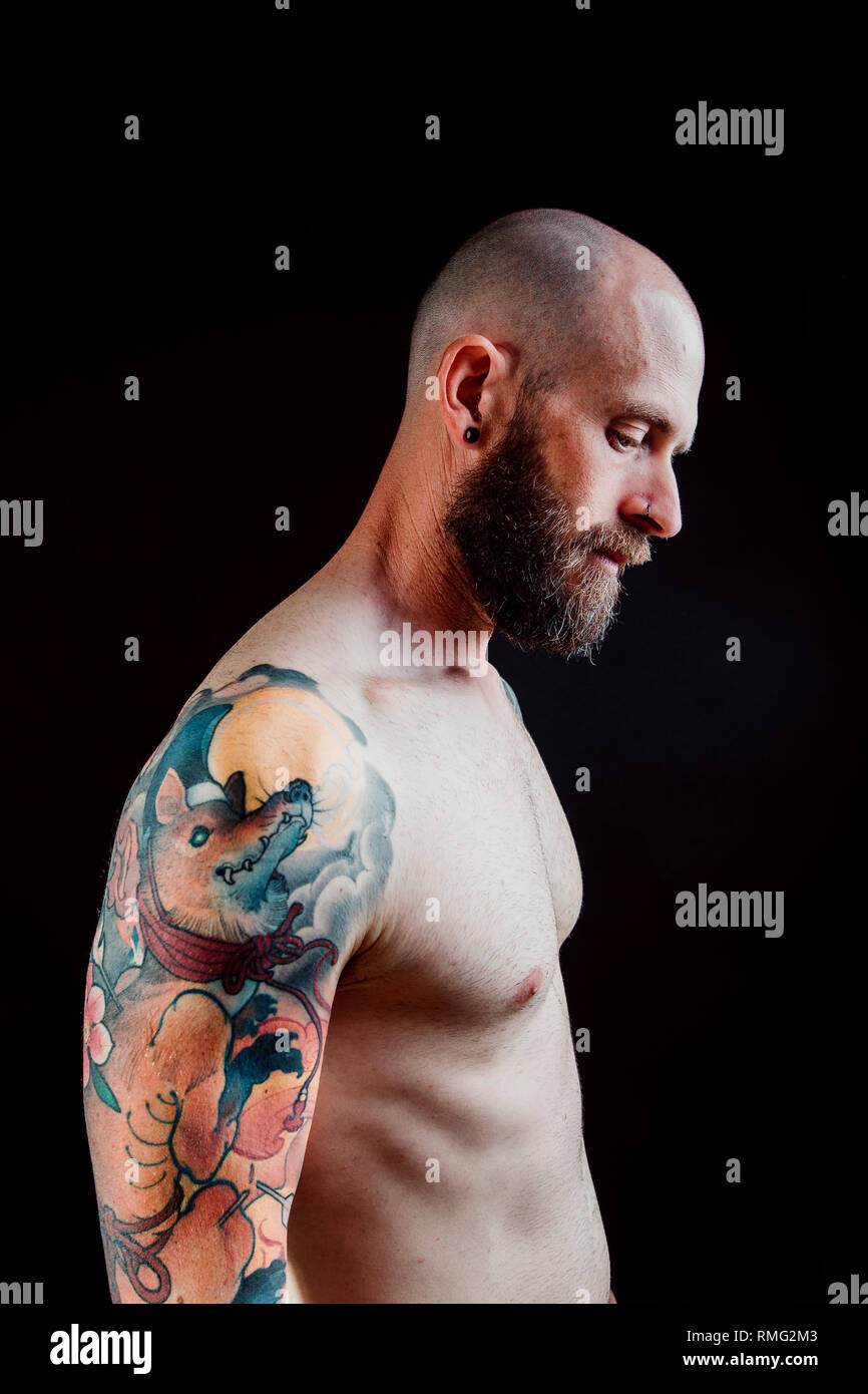 Side View Of Shirtless Bald Serious Hipster With Tattoos On Arms