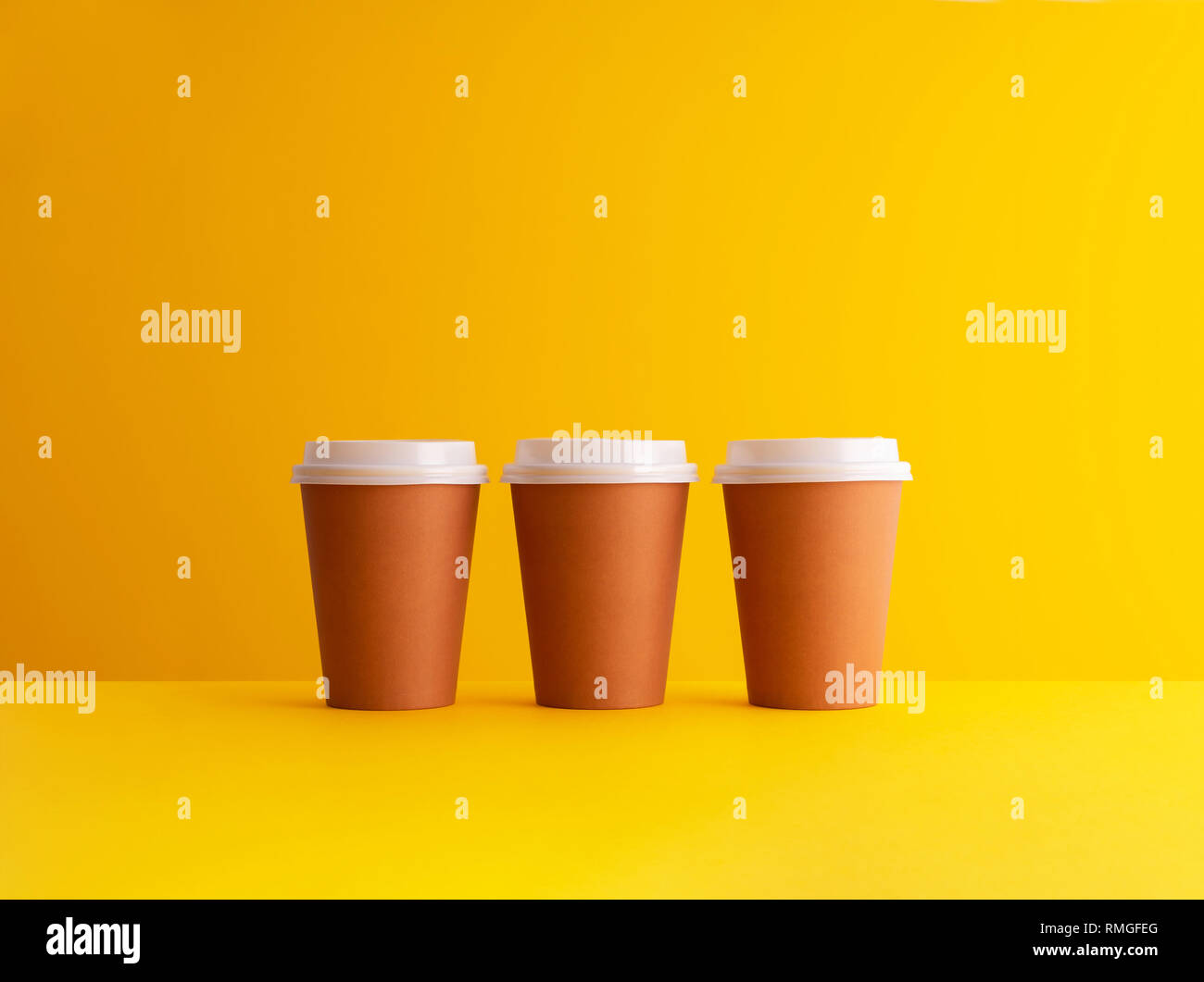 Multiple disposable coffee cups organized in a row over yellow