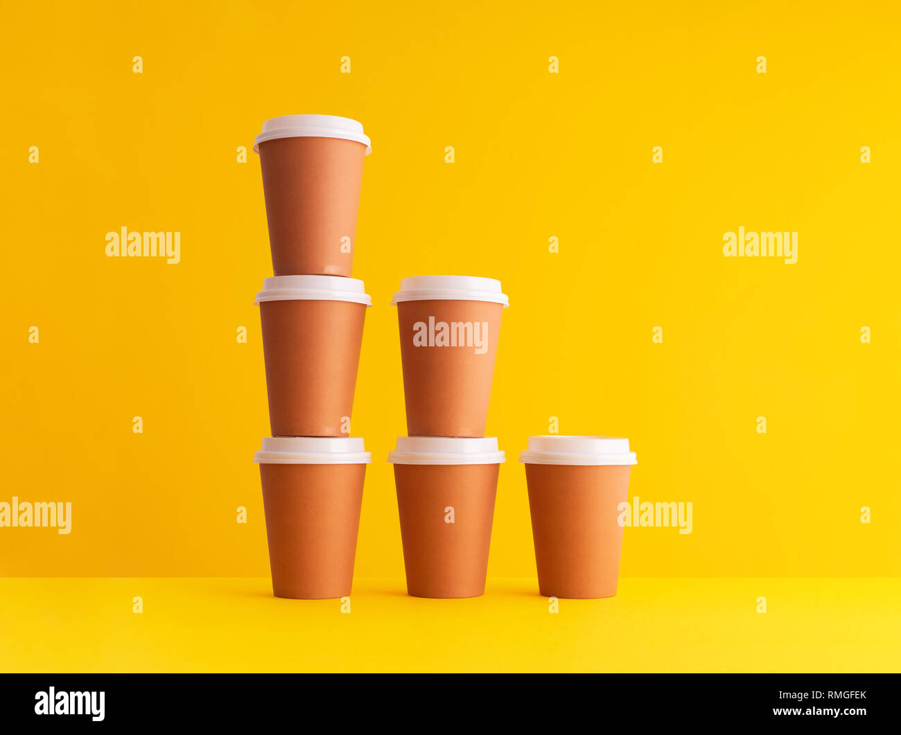 Multiple disposable coffee cups organized in a stack over yellow