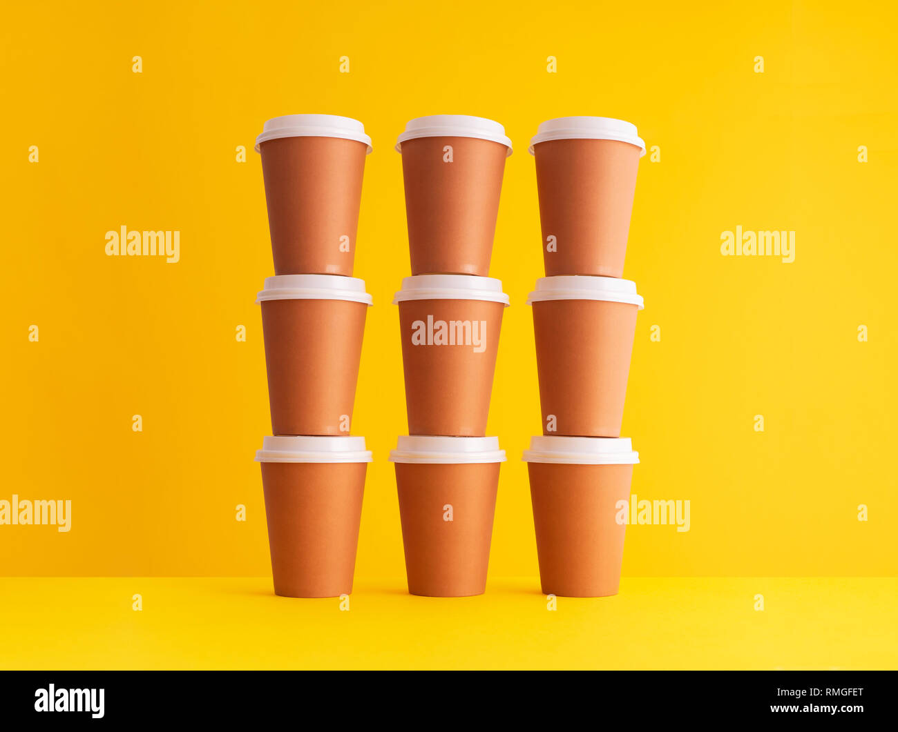 Multiple disposable coffee cups organized in a stack over yellow