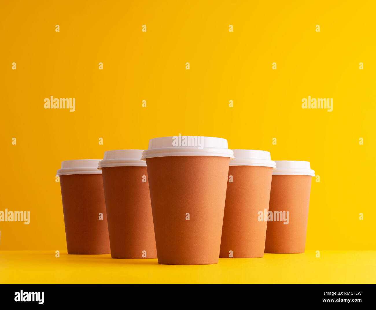 Multiple disposable coffee cups organized in a row over yellow