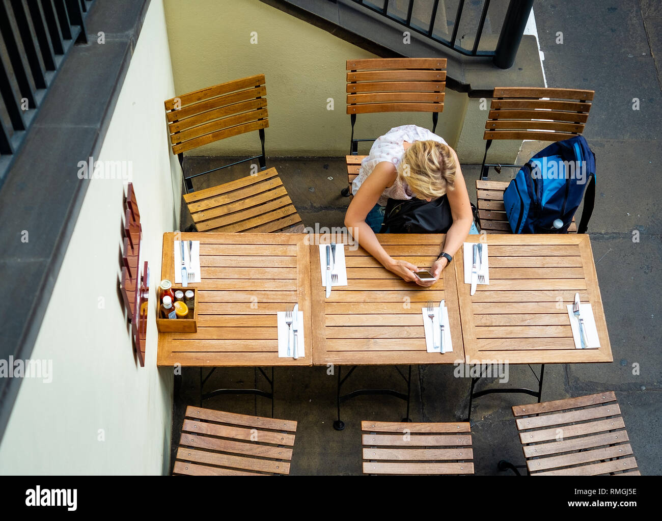 London, England - 2 June 2018: Looking down towards a young lady checking a mobile phone at a restaurant table. Stock Photo