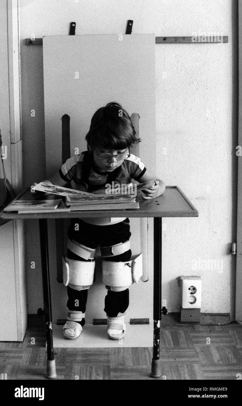 A child reads a picture book in a standing aid in a kindergarten for physically disabled children in Leipzig. The child is tied there for about half an hour. This is to stimulate the circulation and the knees are pushed. Stock Photo