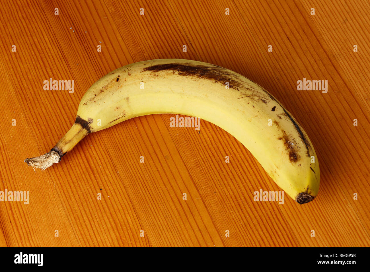 One unpeeled yellow banana on a wooden table top. Stock Photo