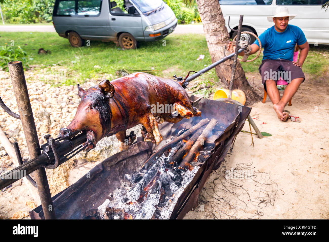 Tongatapu, Tonga - Jan 10 2014: a local native indigenous Polynesian man does a pork barbecue of a piglet on an open fire of a home-made grill made of Stock Photo