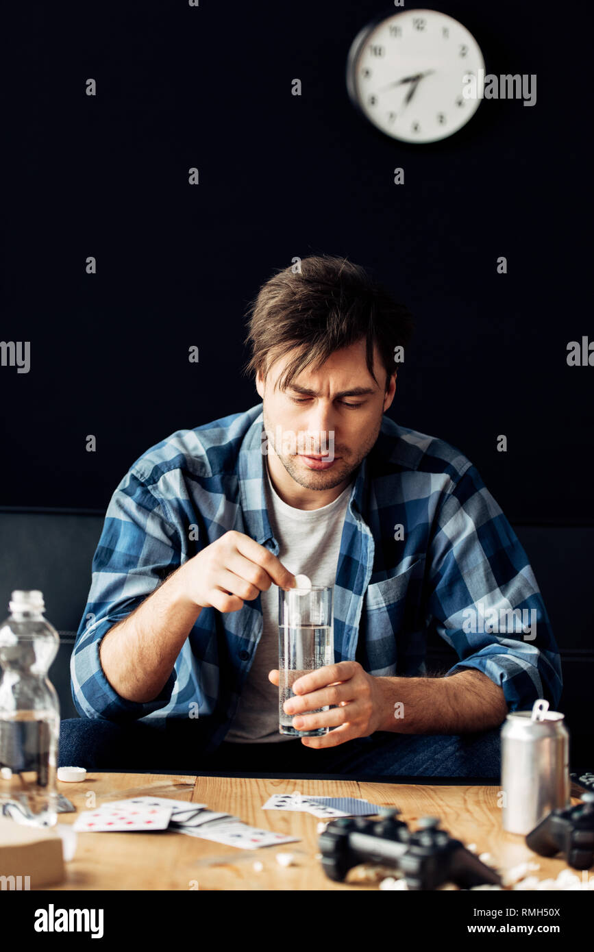 tired man suffering from hangover holding aspirin and glass of water in