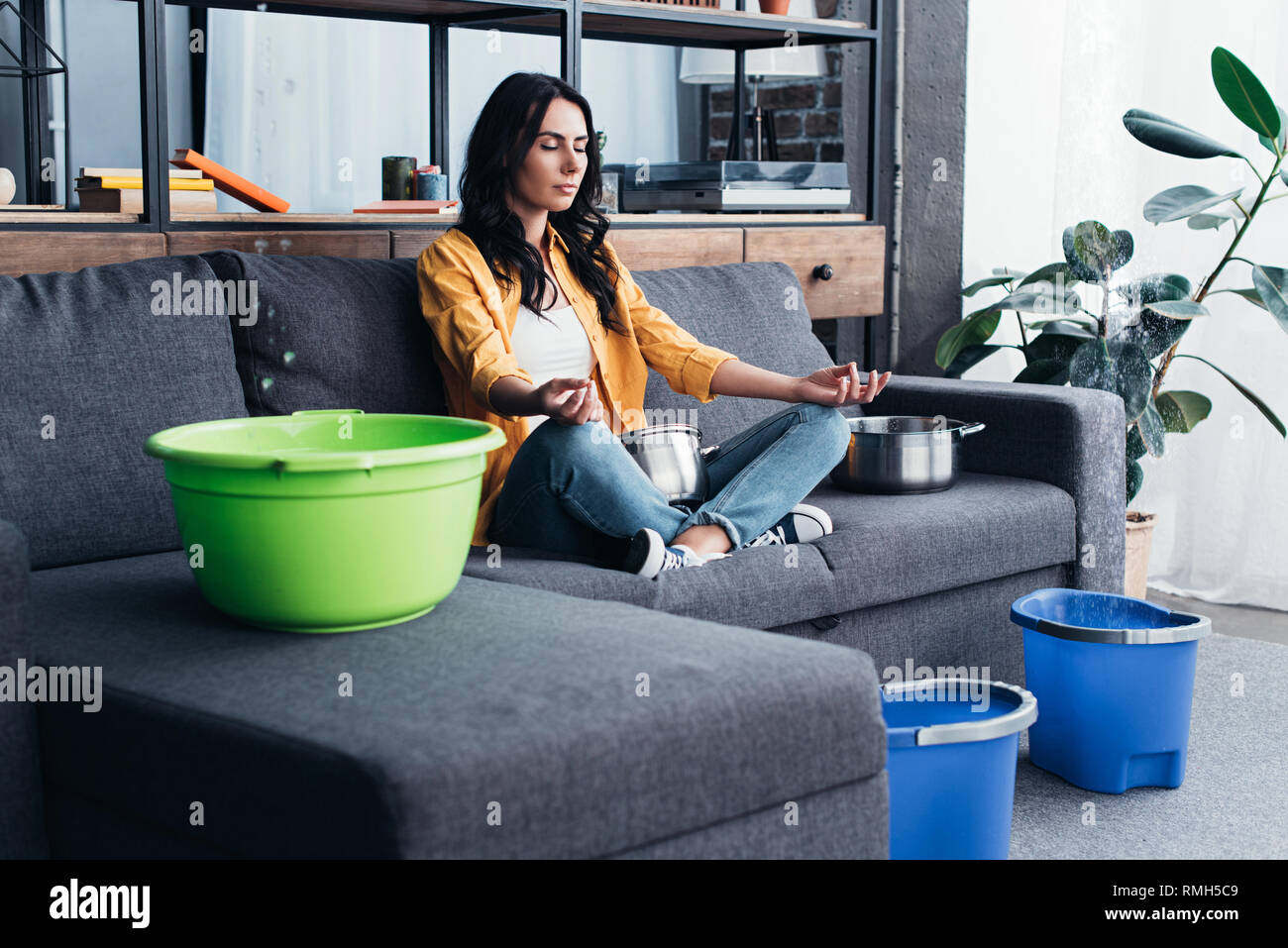 Woman sitting in yoga pose during water damage in living room Stock Photo