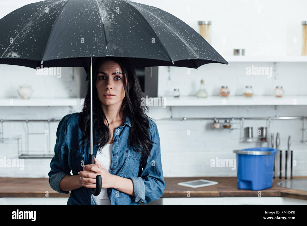 Amazed woman standing under umbrella during leak in kitchen Stock Photo