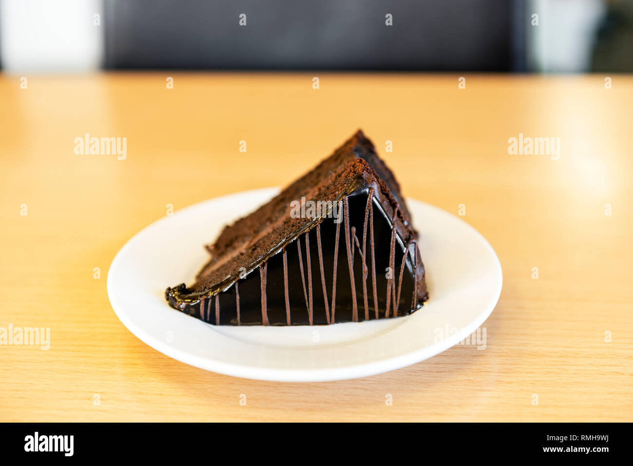 A slice of chocolate cake with icing served on a white plate on an office desk, UK. Stock Photo