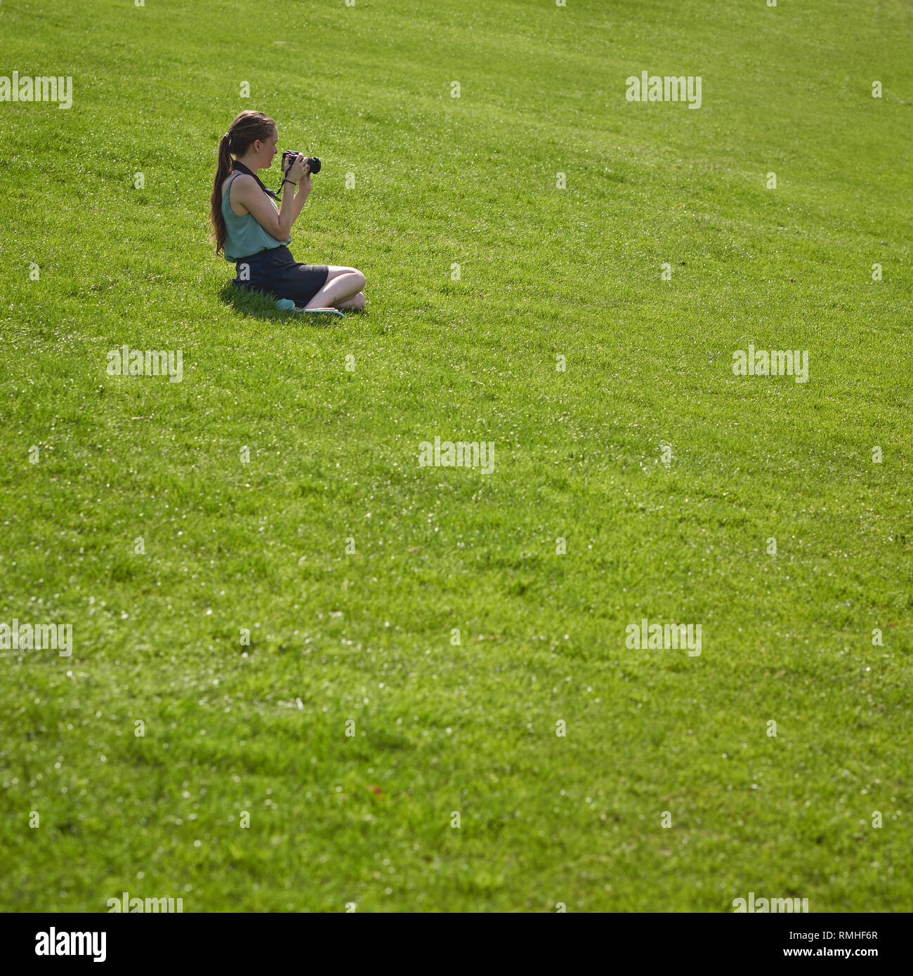 London, UK - June, 2018. A young girl taking photographs while sitting on the grass in a park. Stock Photo