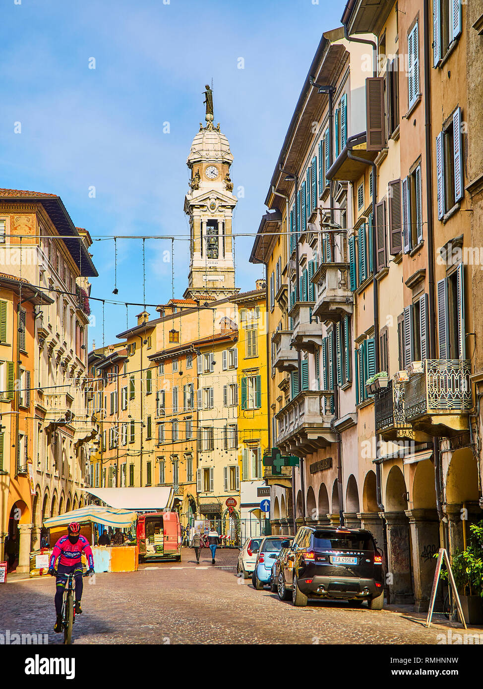 A cyclist  crossing Piazza Pontida square with The Tower Bell of The Basilica of St. Alexander in Column in the background, at Citta Bassa, Bergamo. Stock Photo