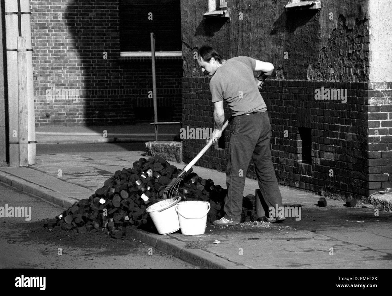 GDR : A man is shoveling lignite / brown coal off the street in Bitterfeld , in February 1990 Stock Photo