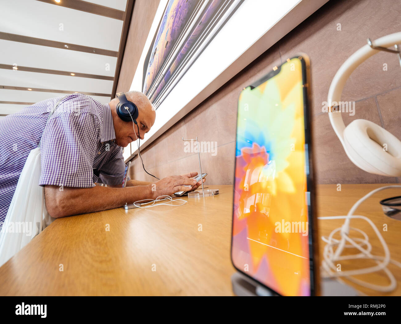 STRASBOURG, FRANCE - SEP 21, 2018: Funny curious senior man testing Apple Beats by Dr Dre headphones with Apple Music on the new iPhone Xs Max smartphones in modern Apple Store - touchscreen  Stock Photo