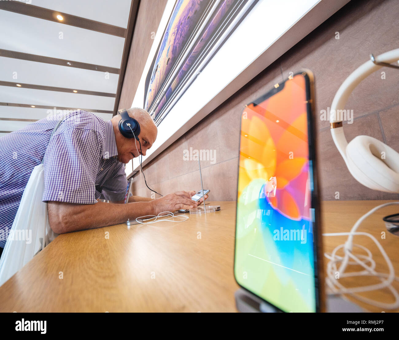 STRASBOURG, FRANCE - SEP 21, 2018: Funny curious caucasian senior man testing Apple Beats by Dr Dre headphones with Apple Music on the new iPhone Xs Max smartphones in modern Apple Store  Stock Photo