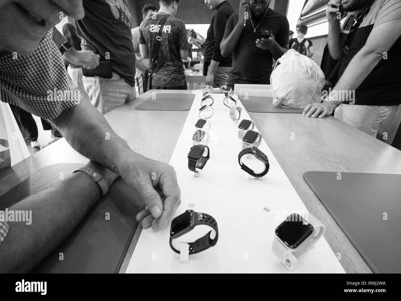 STRASBOURG, FRANCE - SEP 21, 2018: Curious senior man testing the Nike Apple Watch Series 4 GPS LTE smartwatch in Apple Store with customers silhouettes in background black and white Stock Photo
