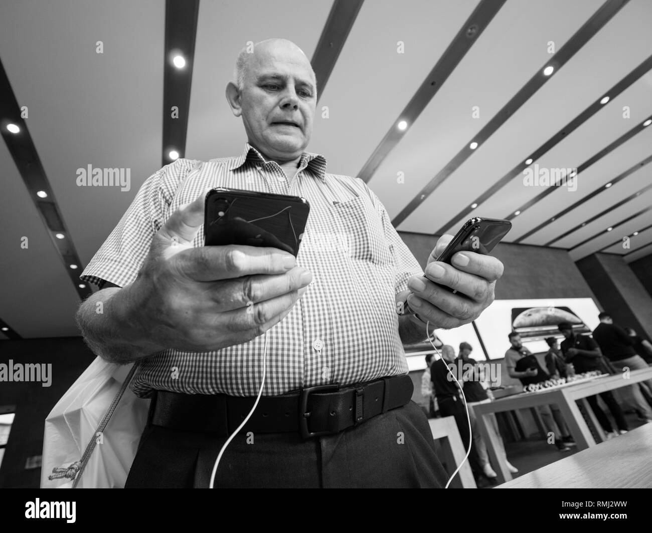 STRASBOURG, FRANCE - SEP 21, 2018: Apple Store with ahppy senior male customer compare buying admiring the new latest iPhone Xs and Xs Max pre order for Xr and Watch Series 4 wearable - black and white Stock Photo