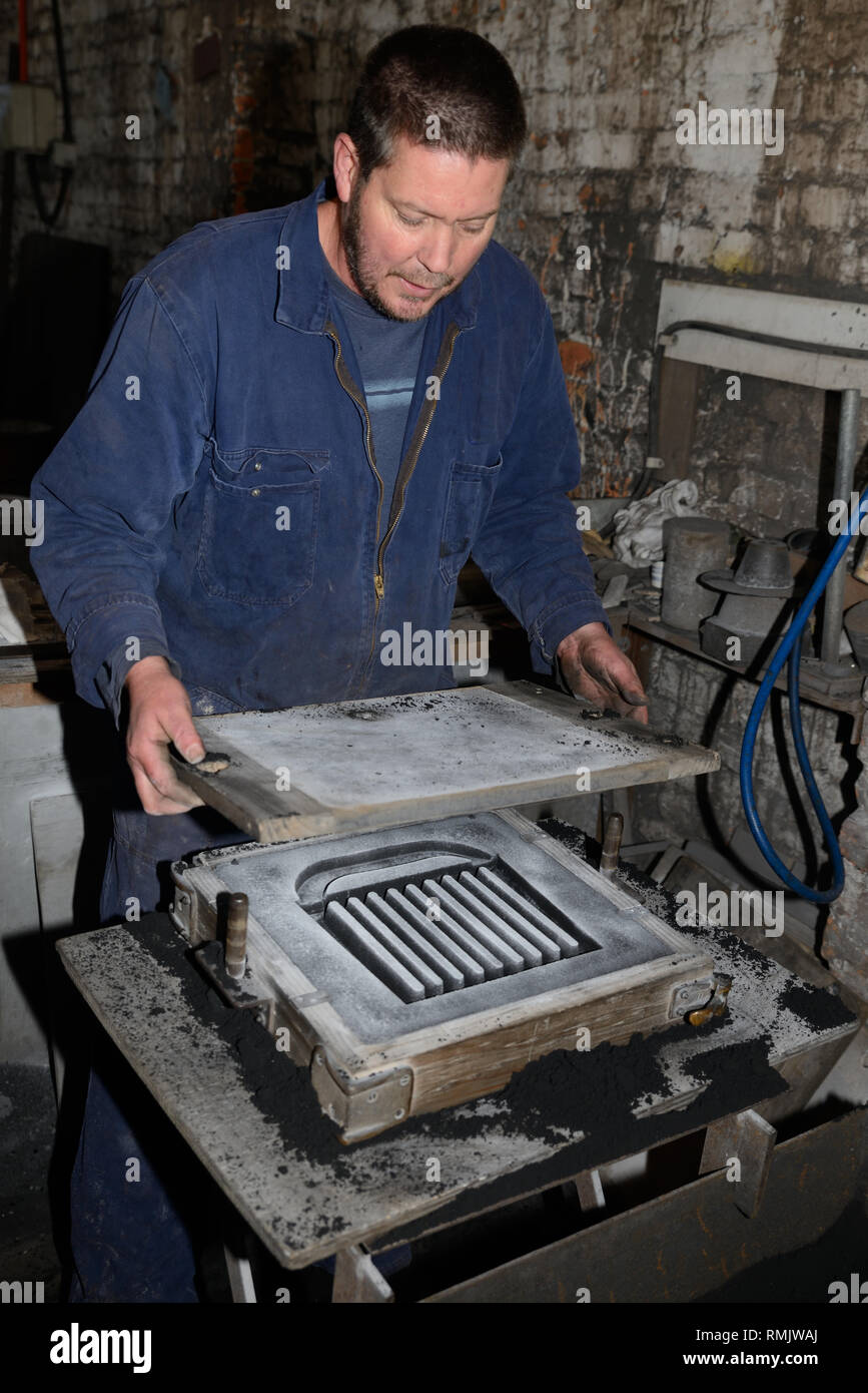A foundryman separates the two halves of a mould for making a fire grate from molten iron. Stock Photo