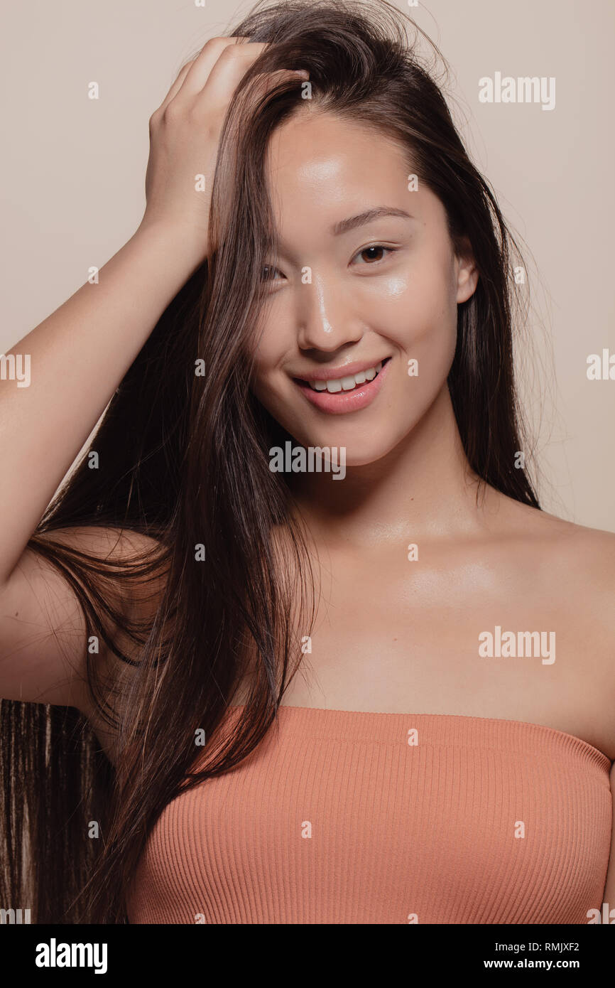 Close-up beauty shot of young pretty girl with natural makeup on beige background. Portrait of korean female model looking at camera and smiling. Stock Photo