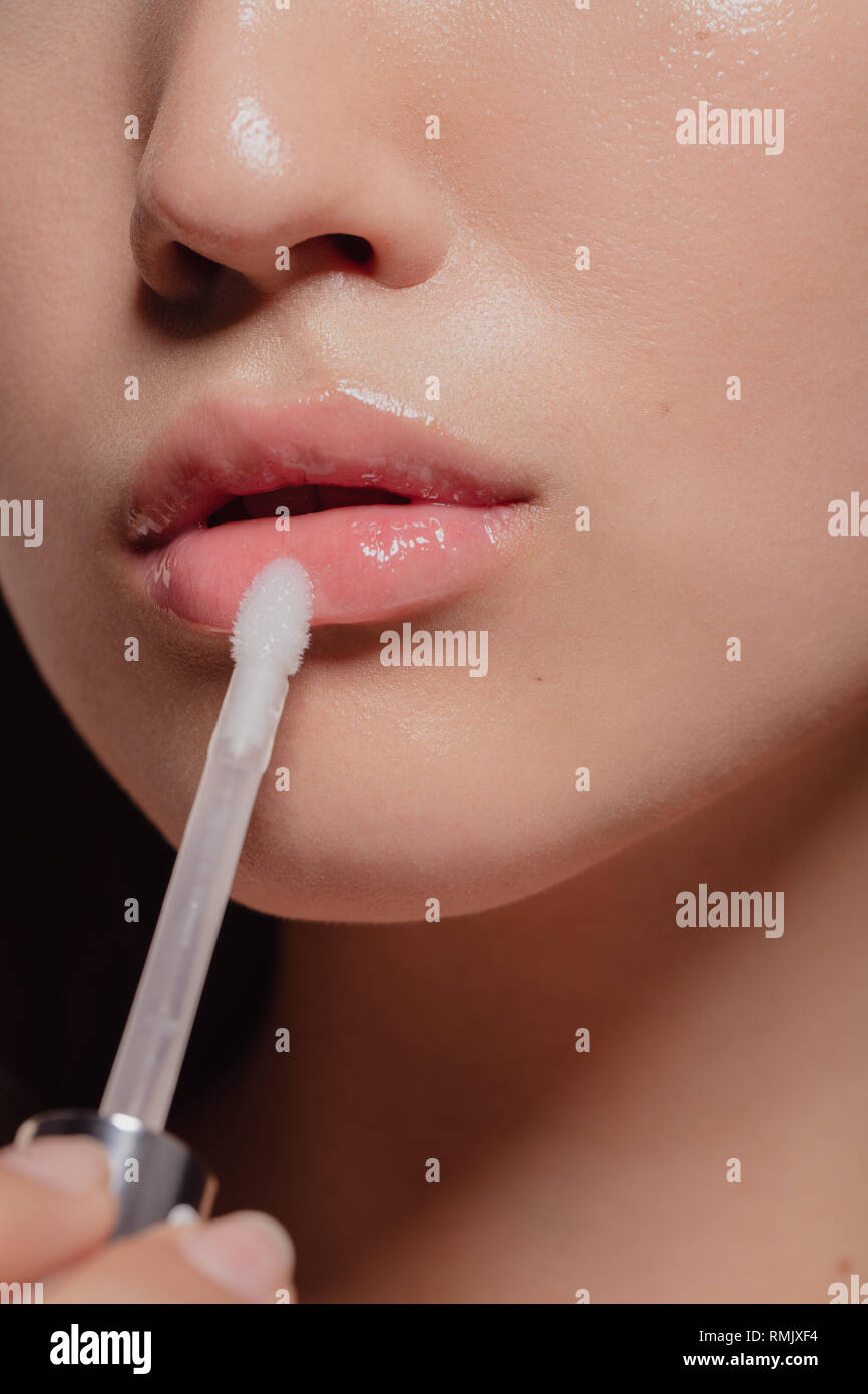 Close up of woman applying transparent lip gloss with applicator. Cropped shot of girl doing makeup on her lips. Stock Photo