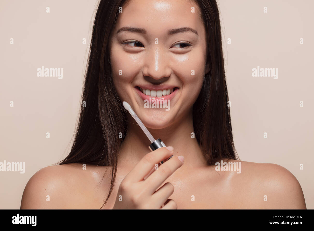 Close up of smiling young woman doing make up. Korean female model with make up applicator looking away and smiling. Stock Photo