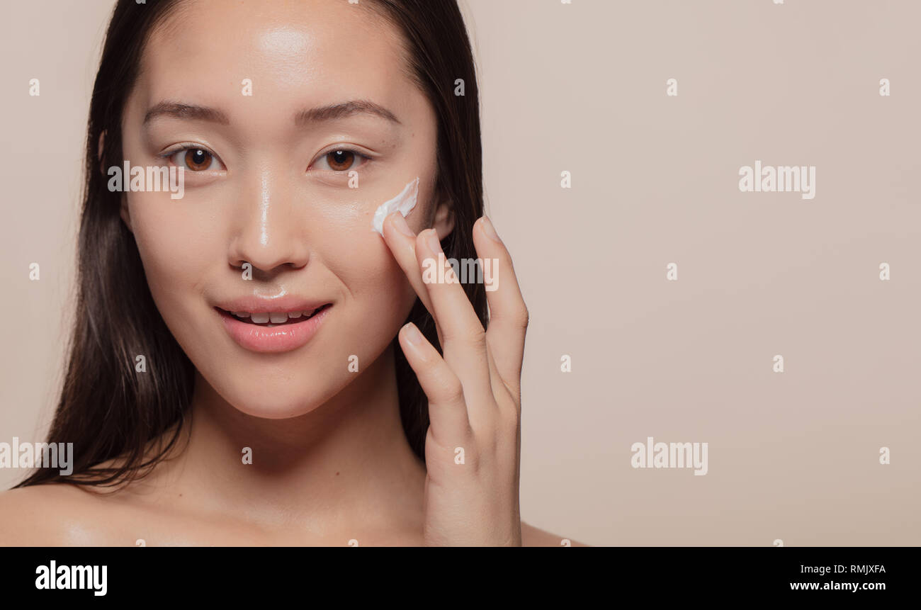 Close up of a asian woman applying moisturizer to her pretty face. Female model putting cream on her glowing face skin. Stock Photo