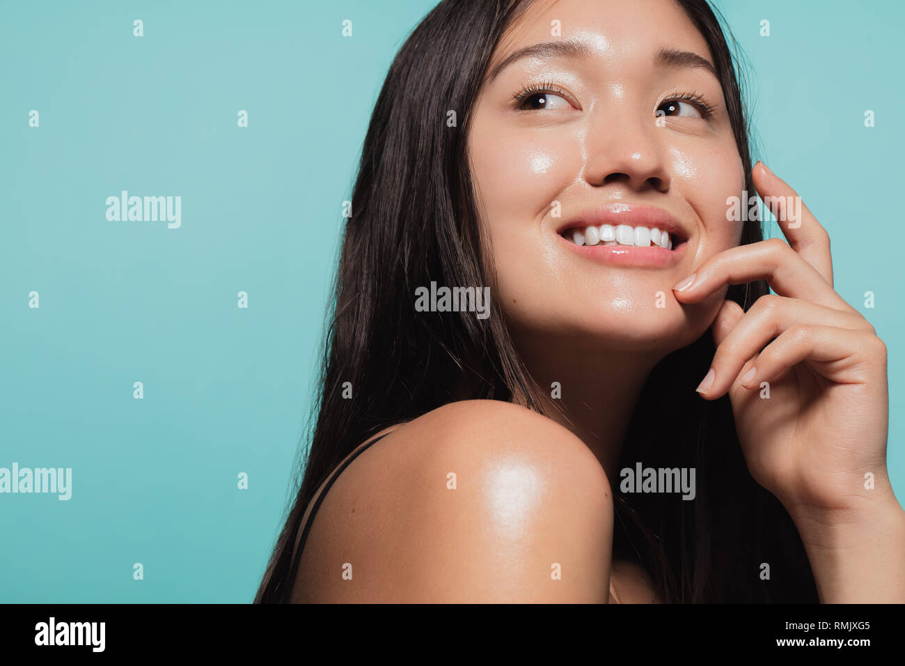 Close up of cute asian girl with glowing skin against blue background. Beautiful face of girl with fresh healthy skin. Stock Photo