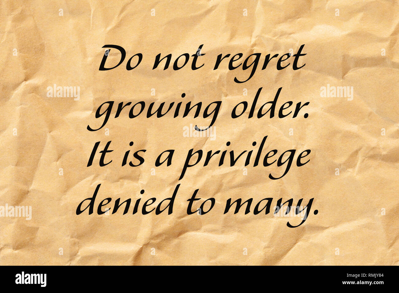 Do not regret growing older. It is a privilege denied to many. Positive aging quote written on crumpled brown paper. Stock Photo