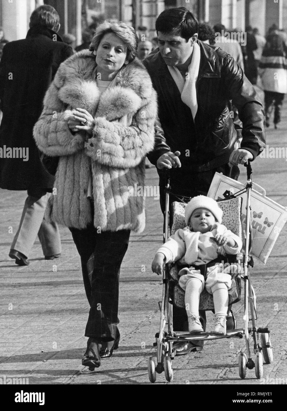Baby carriages from all centuries - a couple in a pedestrian zone while strolling through the city. The man pushes the stroller. Stock Photo