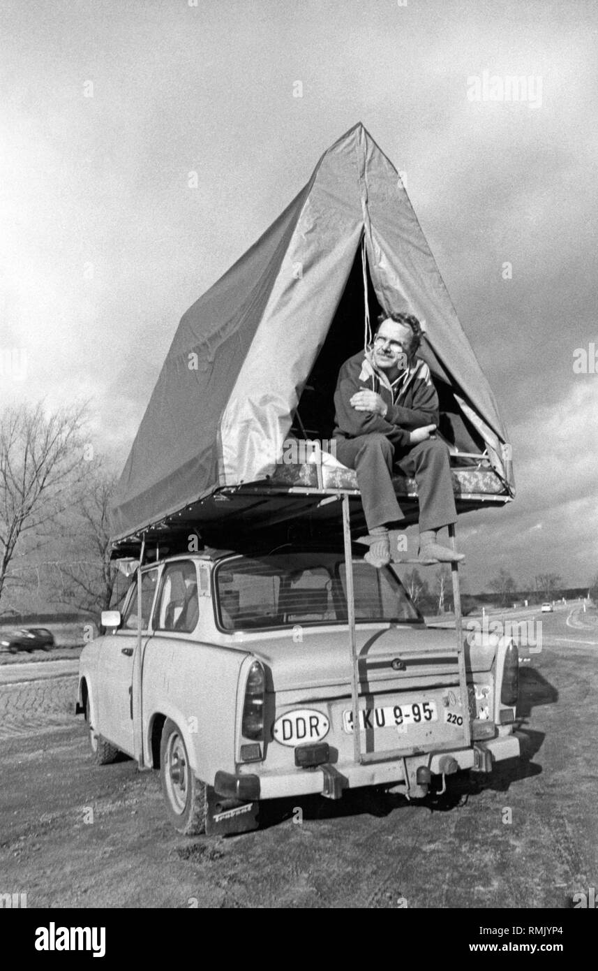 A man sits in a Mueller roof tent, which is mounted on a Trabant 601, on the edge of the transit highway to Berlin. Stock Photo
