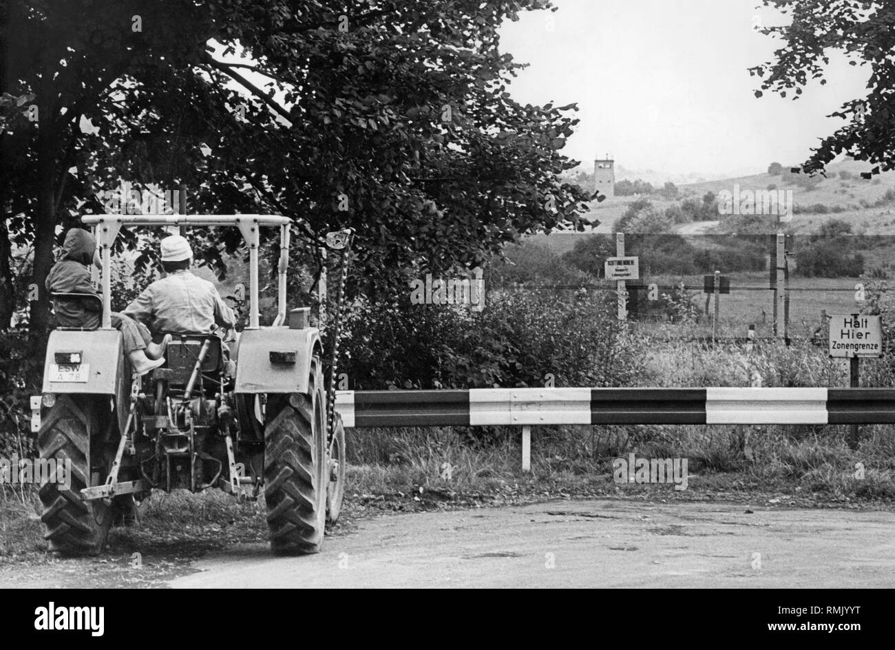 A tractor in front of the inter- German border in Hessian Rittmannshausen, district of Ringau. To the right, a warning sign of the Federal Border Guard. In the background, a watchtower of the GDR border installations. Stock Photo
