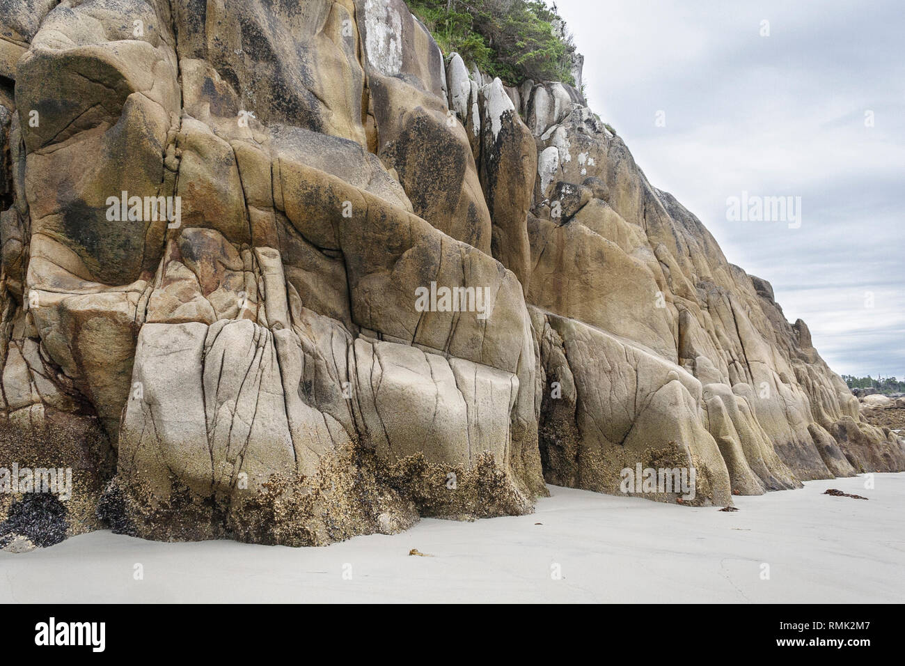 Eroded granite bluffs rise steeply at the edge of a sandy beach on the exposed outer shore of CalvertIisland, on British Columbia's Central Coast. Stock Photo