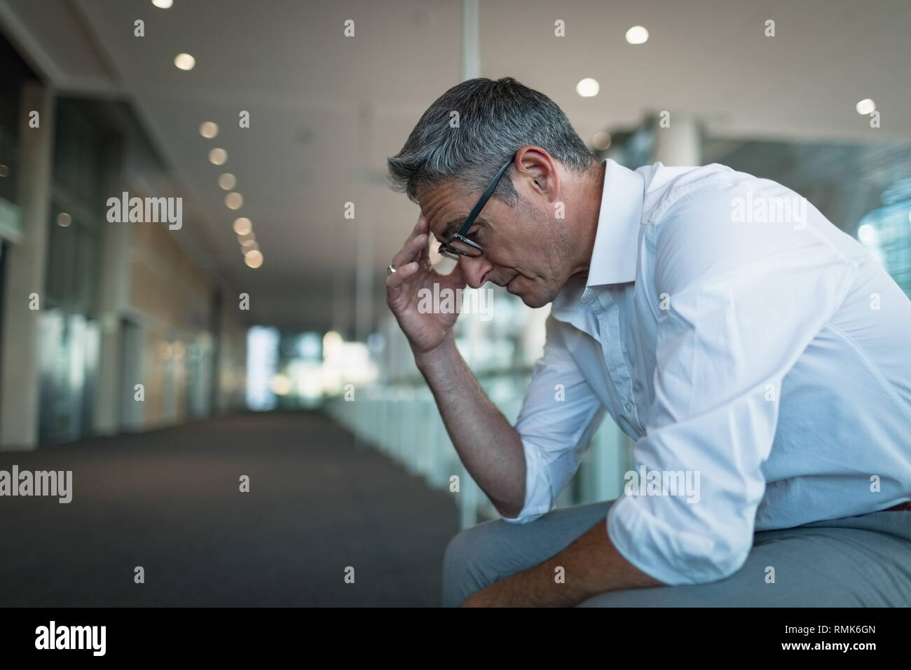 Frustrated businessman sitting in office corridor Stock Photo