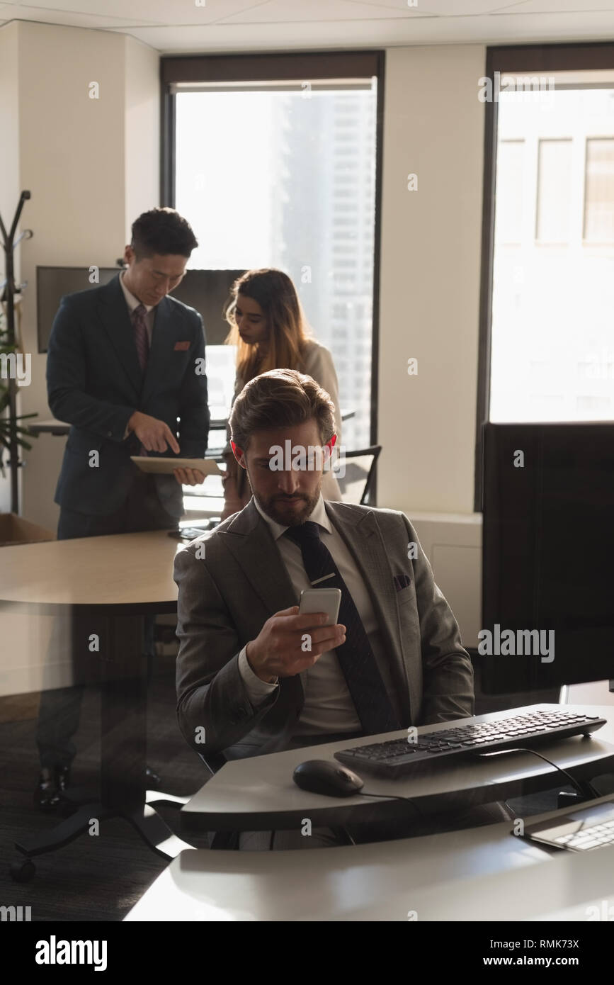 Man using mobile phone while coworkers discussing over digital tablet Stock Photo