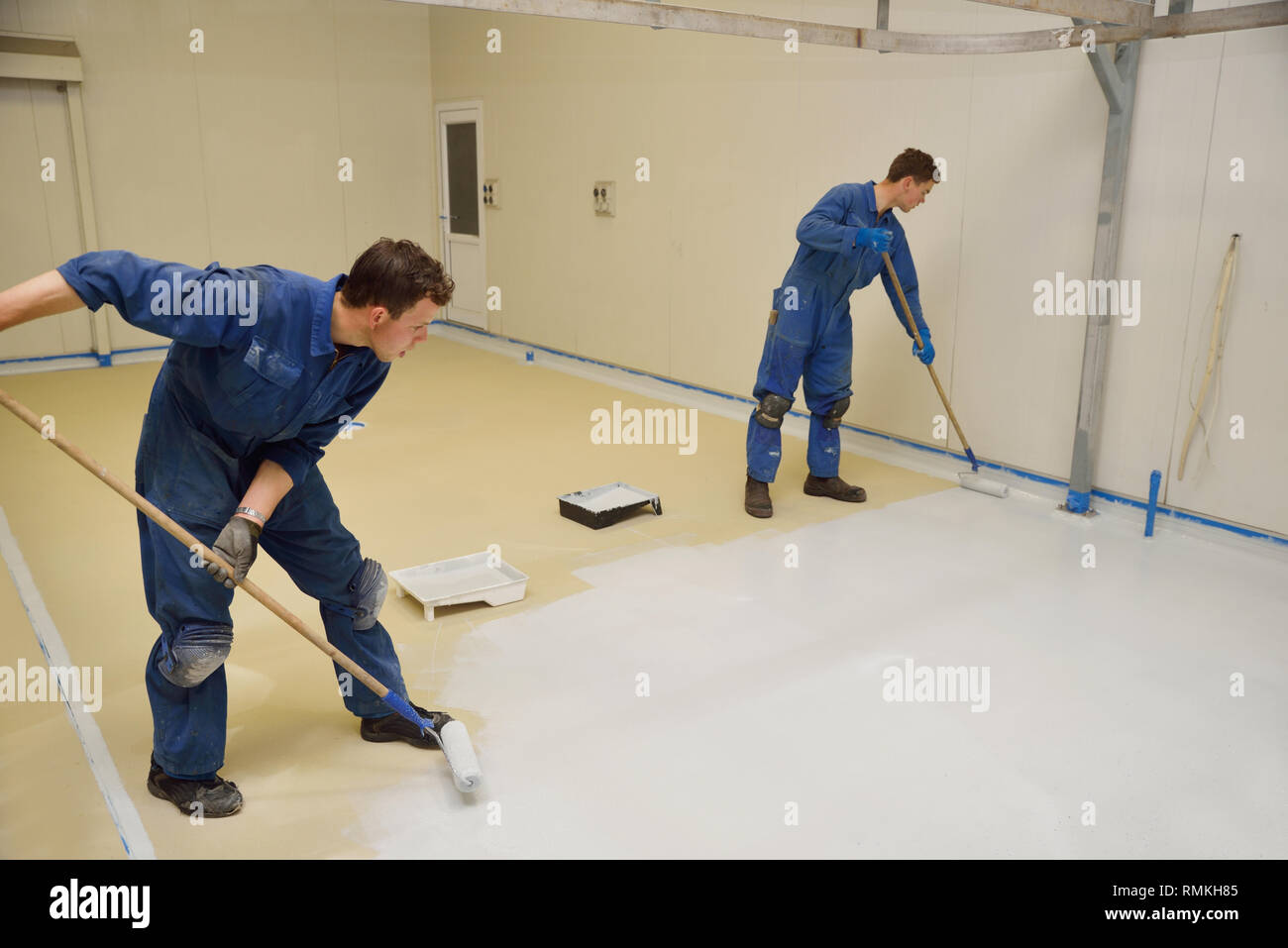 tradesmen rolling final coat of epoxy product on the floor of an industrial building Stock Photo