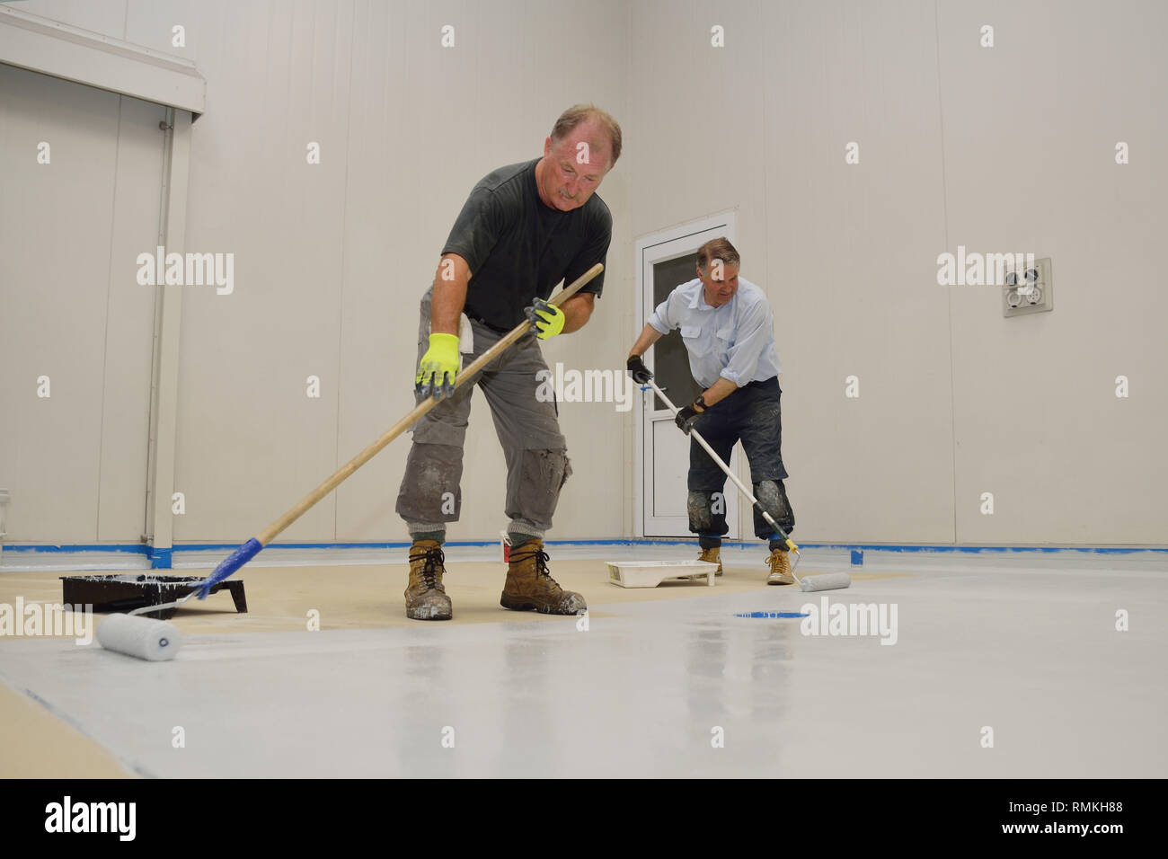 tradesmen rolling final coat of epoxy product on the floor of an industrial building Stock Photo