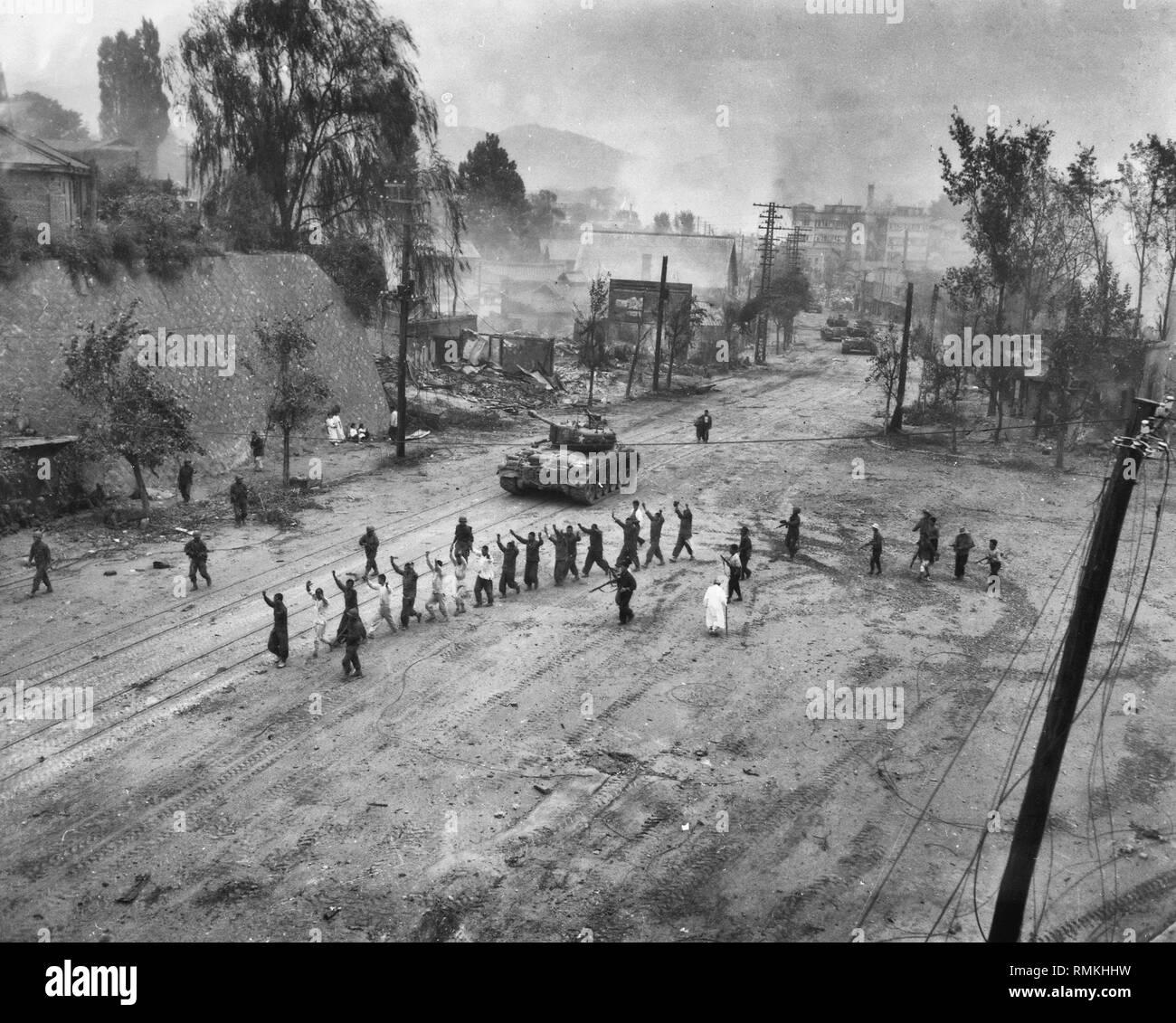 A U.S. Marine tank follows a line of prisoners of war down a village street, Korean War, September 1950 Stock Photo