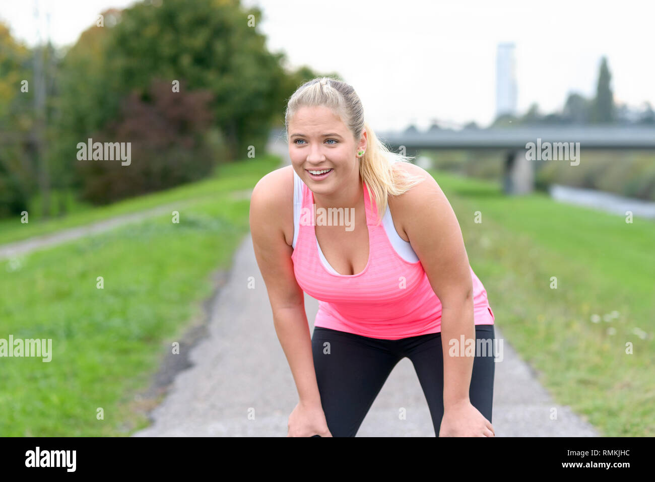 Blonde smiling woman holding knees after jogging along river Stock