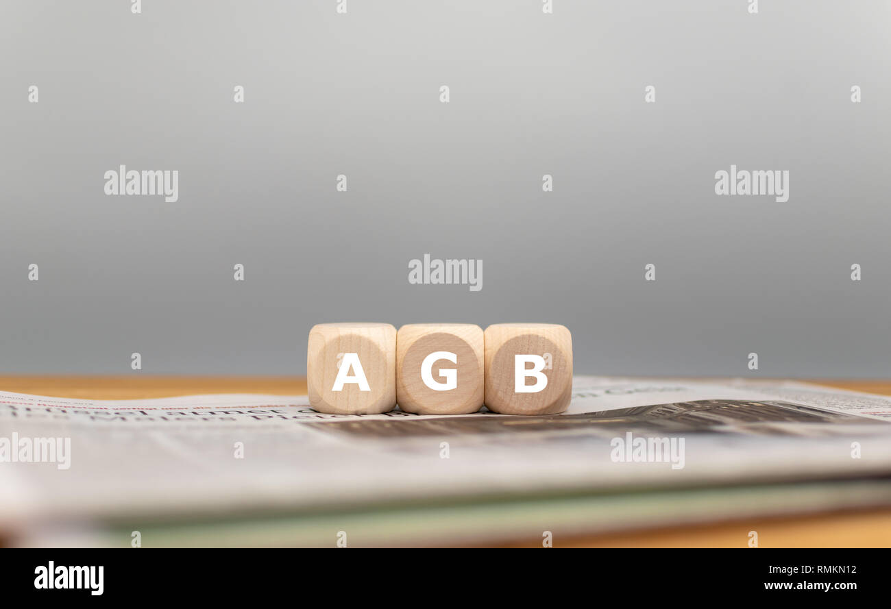 Dice form the German expression AGB (' general terms and conditions' in English) in front of a grey background on a newspaper. Stock Photo