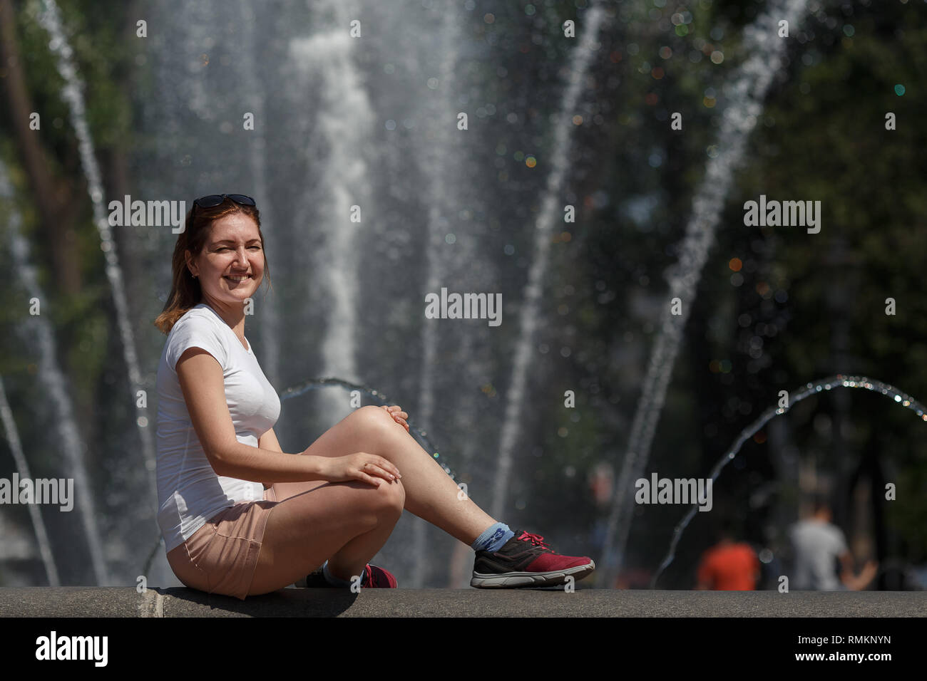 Beautiful woman sitting on the fountain background Stock Photo - Alamy