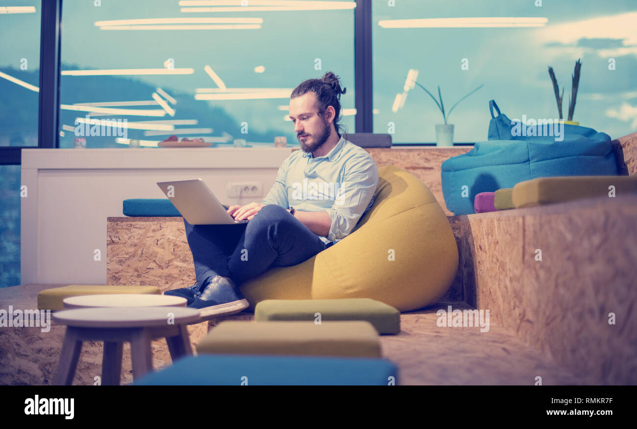 software developer writing programming code using laptop computer while sitting on lazy bag in modern startup office Stock Photo
