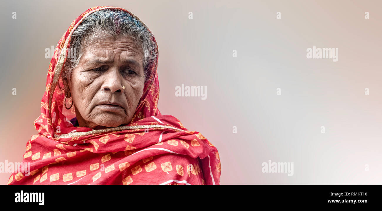 Beautiful photo of Old Aged Indian Woman farmer in her late 70s wearing red robe, in sad mood, because of poor harvest and losing her valuable assets Stock Photo