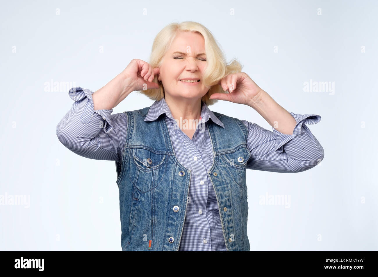 unhappy stressed out senior female making wry face, plugging ears with fingers Stock Photo