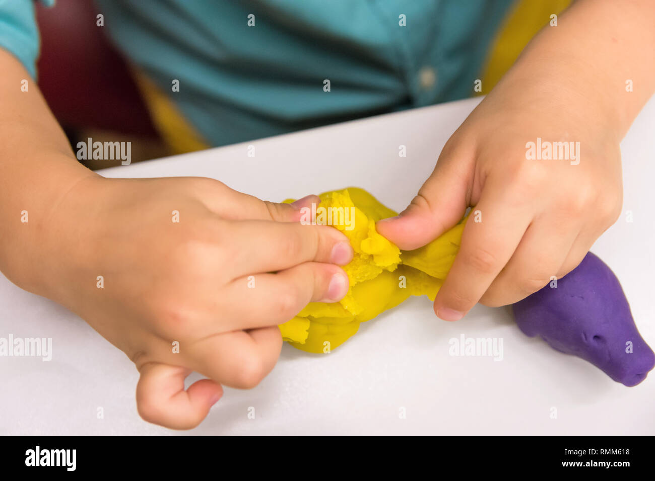 Four year old caucasian boy makes with hands animal figures from modeling yellow clay on white tabletop. Kids creativity preschool education hobby Stock Photo